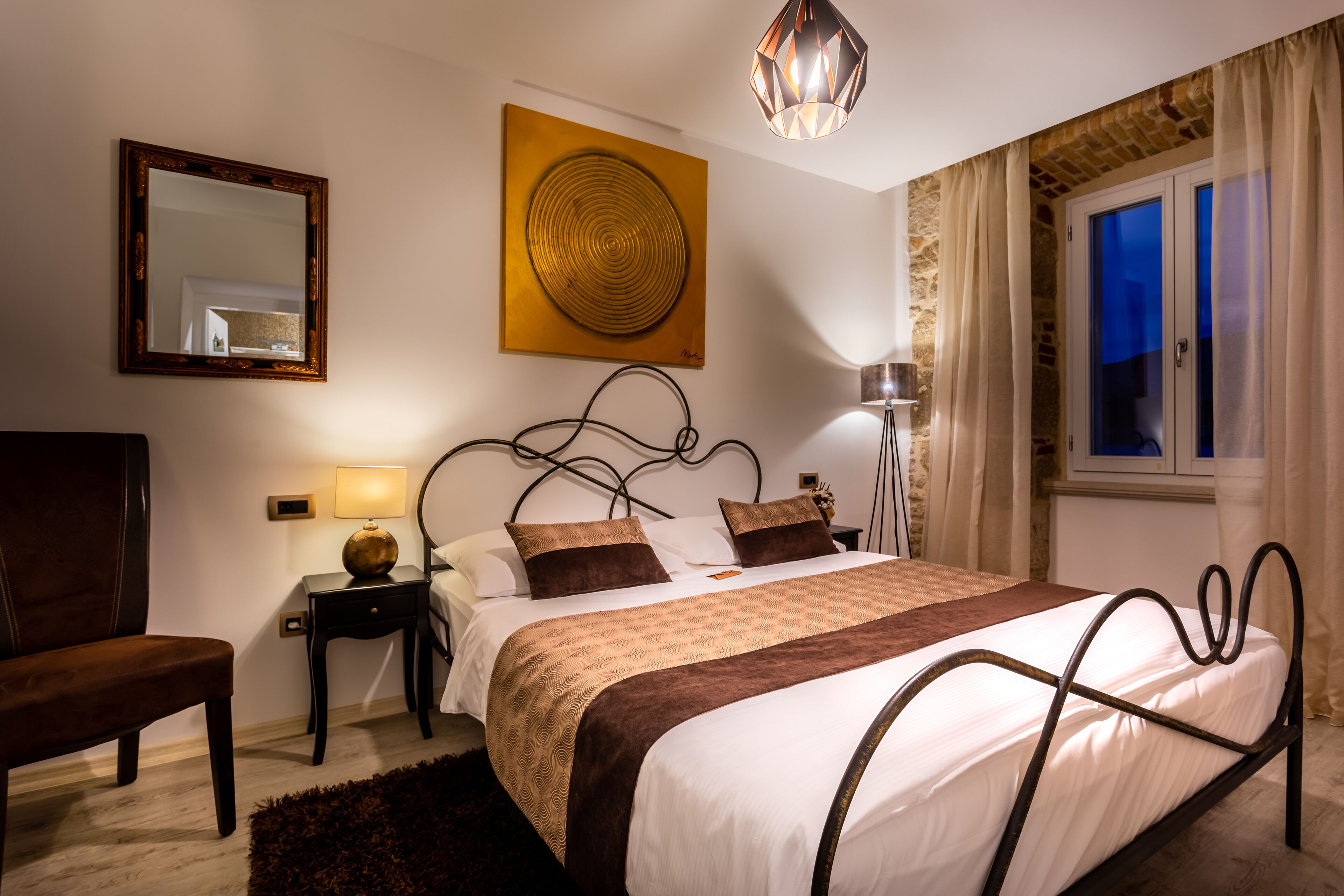A neatly arranged bedroom with a bed, bedside tables, a chair, and a large window with curtains.