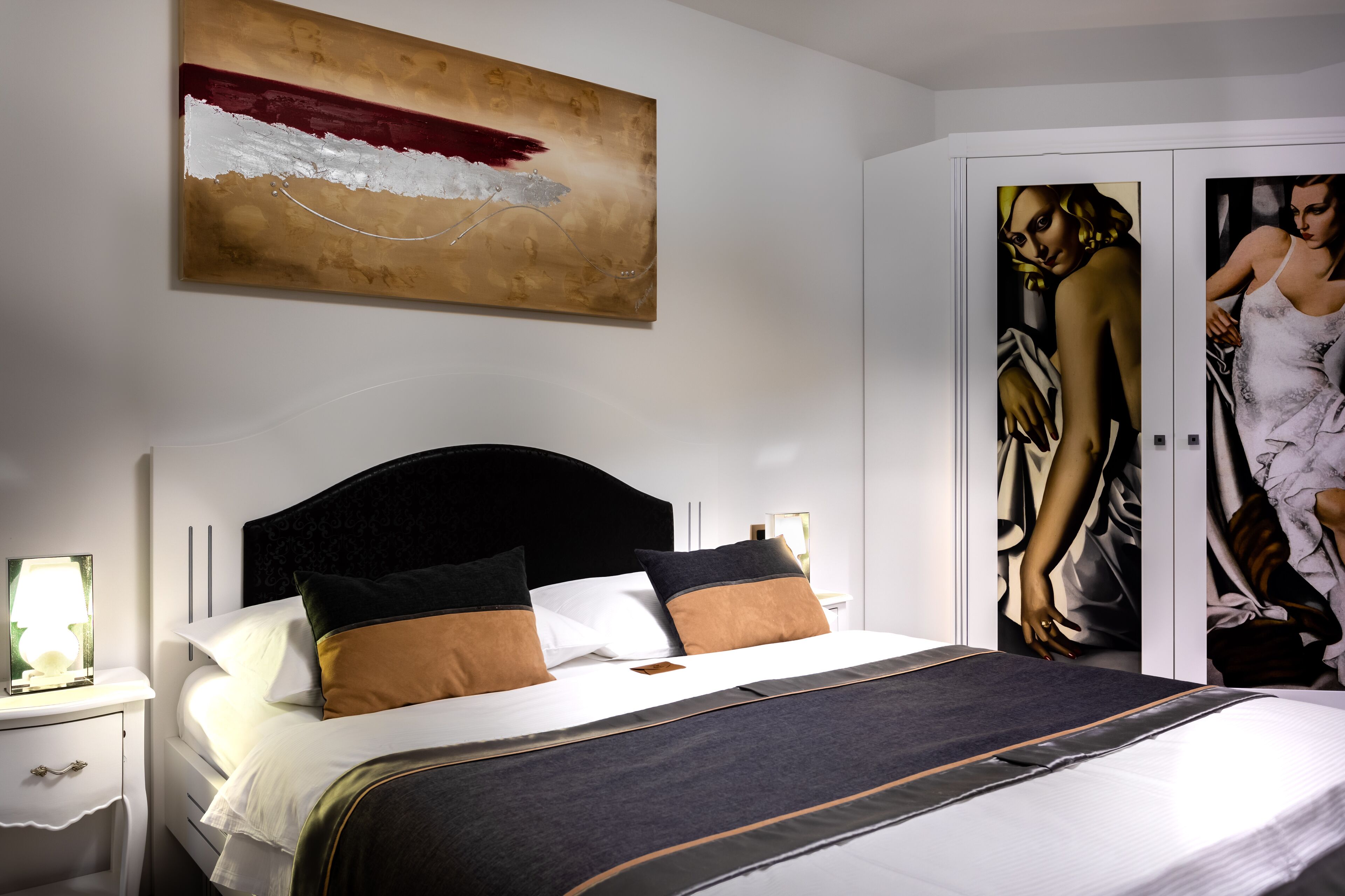 A neatly made bed with a dark headboard, white pillows, and a striped blanket. A large abstract painting is on the wall above the bed.