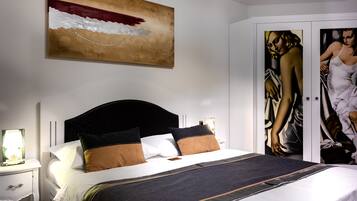 A neatly made bed with a dark headboard, white pillows, and a striped blanket. A large abstract painting is on the wall above the bed.