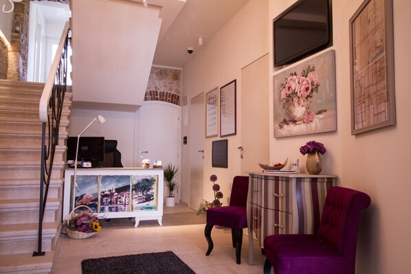 A spacious living area with a staircase, a white cabinet with artwork, a purple armchair, and a small table with a vase of flowers. - Heritage hotel Forza (Baska)
