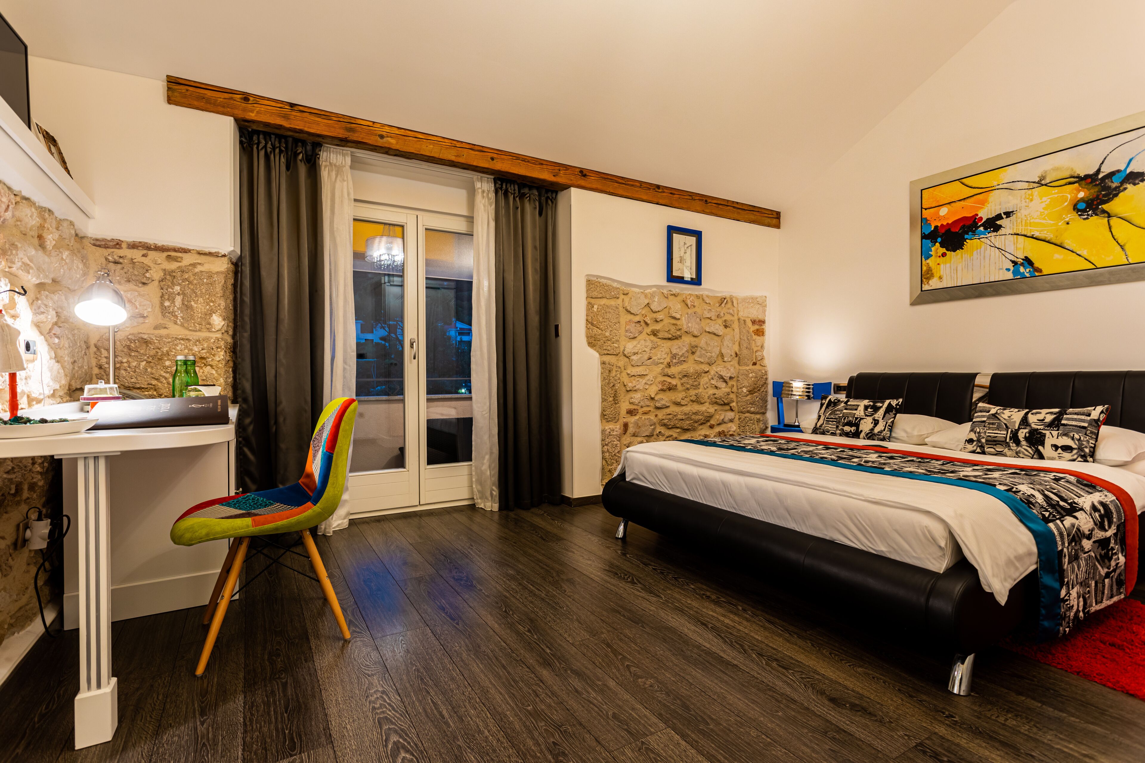 Ein Schlafzimmer mit einem Bett, einem Schreibtisch, einem bunten Stuhl und einer Steinsäule.