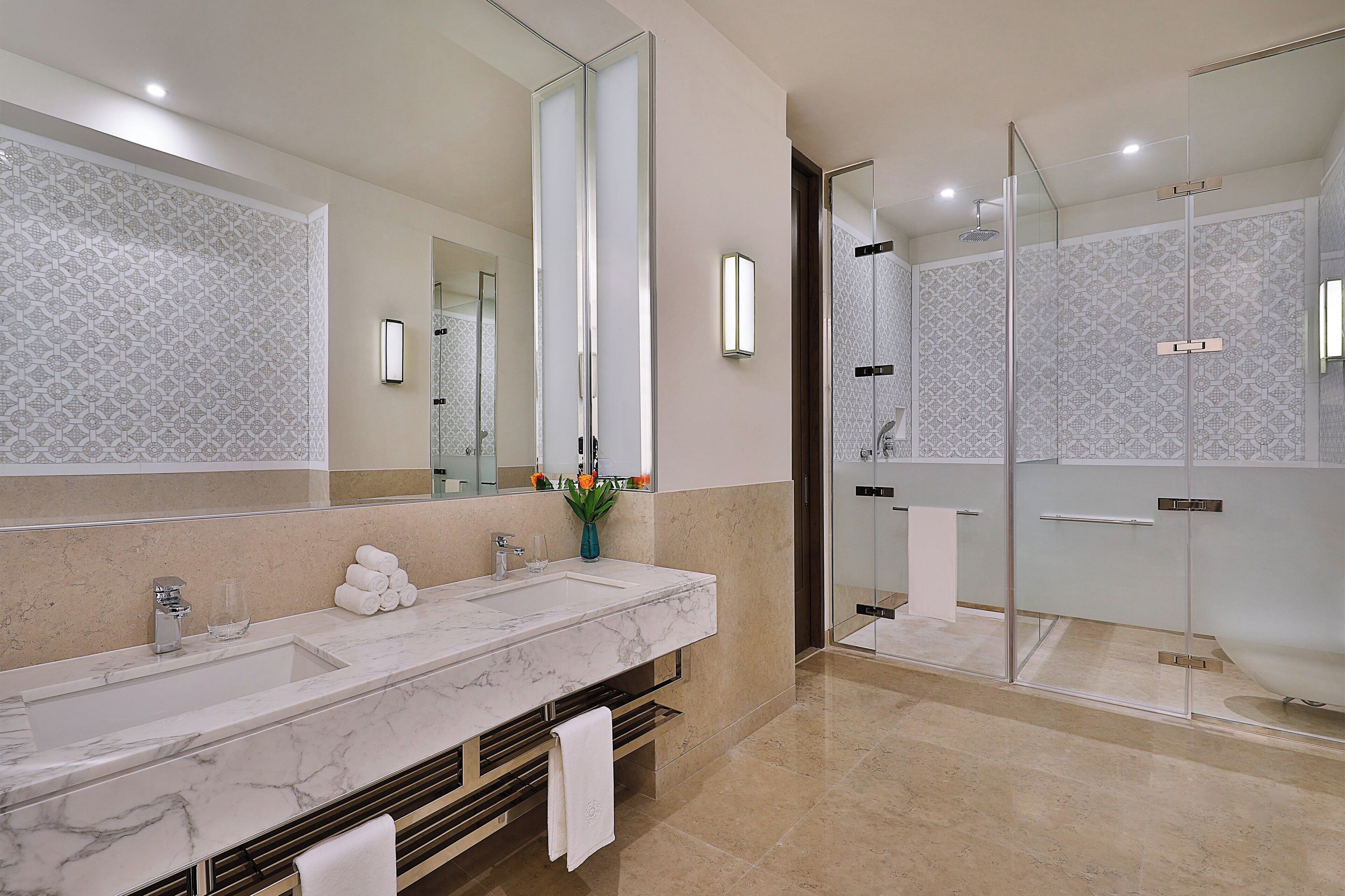 A modern bathroom with a marble sink, a glass shower enclosure, and a large mirror.