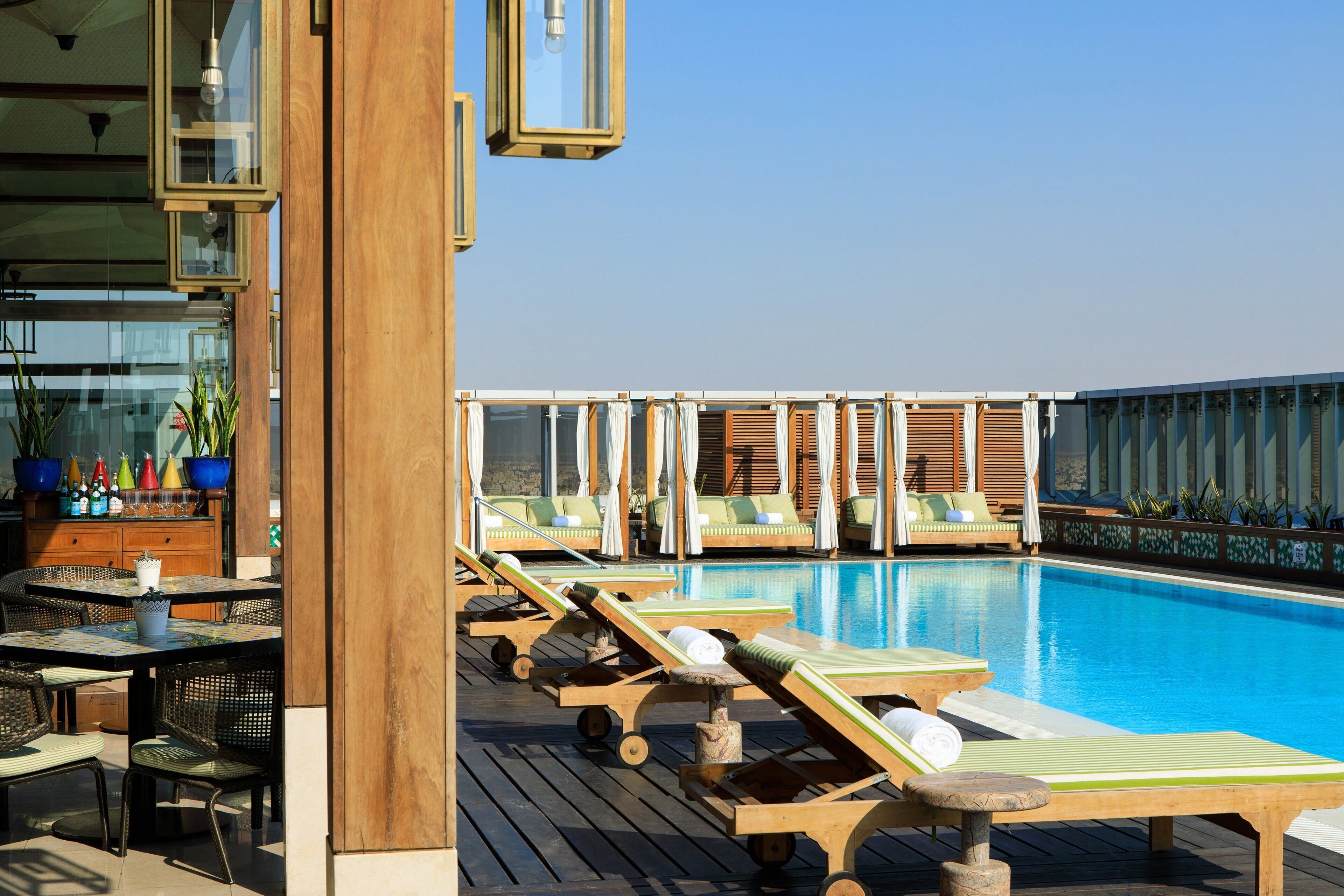 A rooftop pool area with lounge chairs, a dining table with chairs, and a wooden deck.