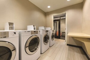 A laundry room with three front-loading washing machines, a control panel, and a wooden counter.