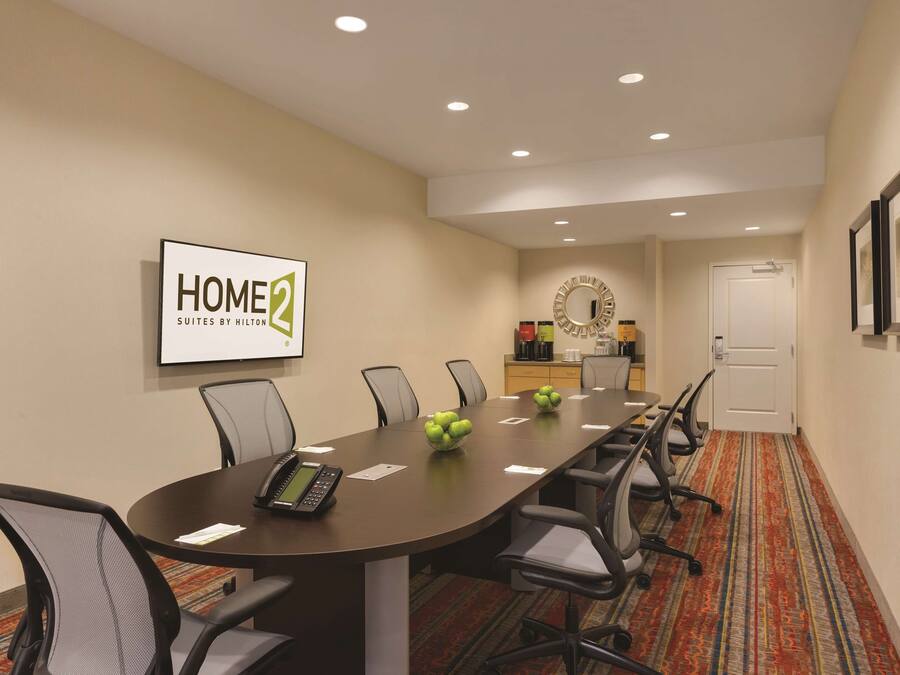 Une salle de conférence équipée d’une longue table, de chaises, d’un écran de projection et d’une enseigne indiquant « HOME2 Suites by Hilton ».