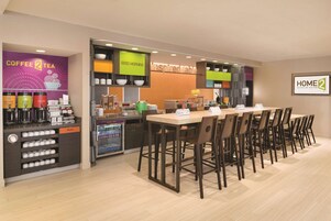 A hotel dining area with a coffee station, a buffet, and a long table with chairs.