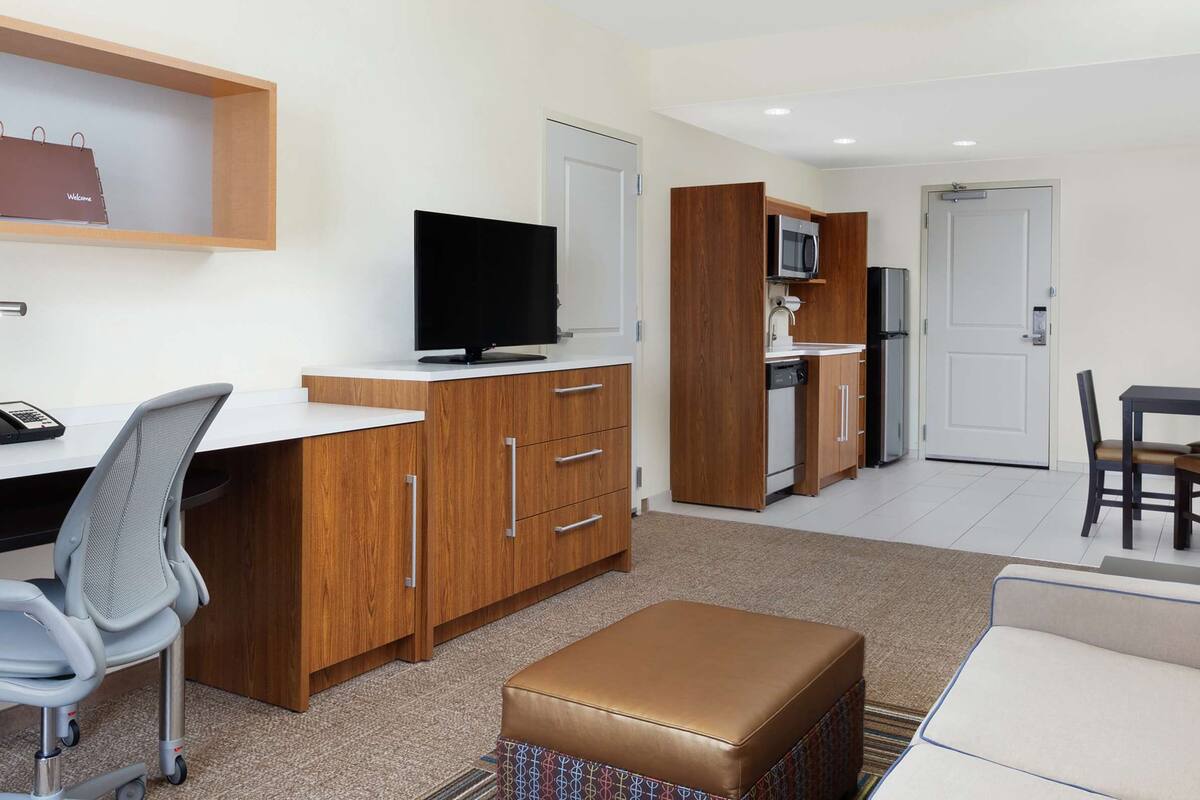 Une chambre d’hôtel moderne équipée d’un bureau, d’un fauteuil de bureau, d’une télévision, d’une kitchenette et d’un canapé.