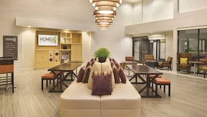 En modern hotellobby med en central sittgrupp, ett litet kök och en matplats.