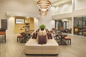 A modern hotel lobby with a central seating area, a kitchenette, and a dining area.