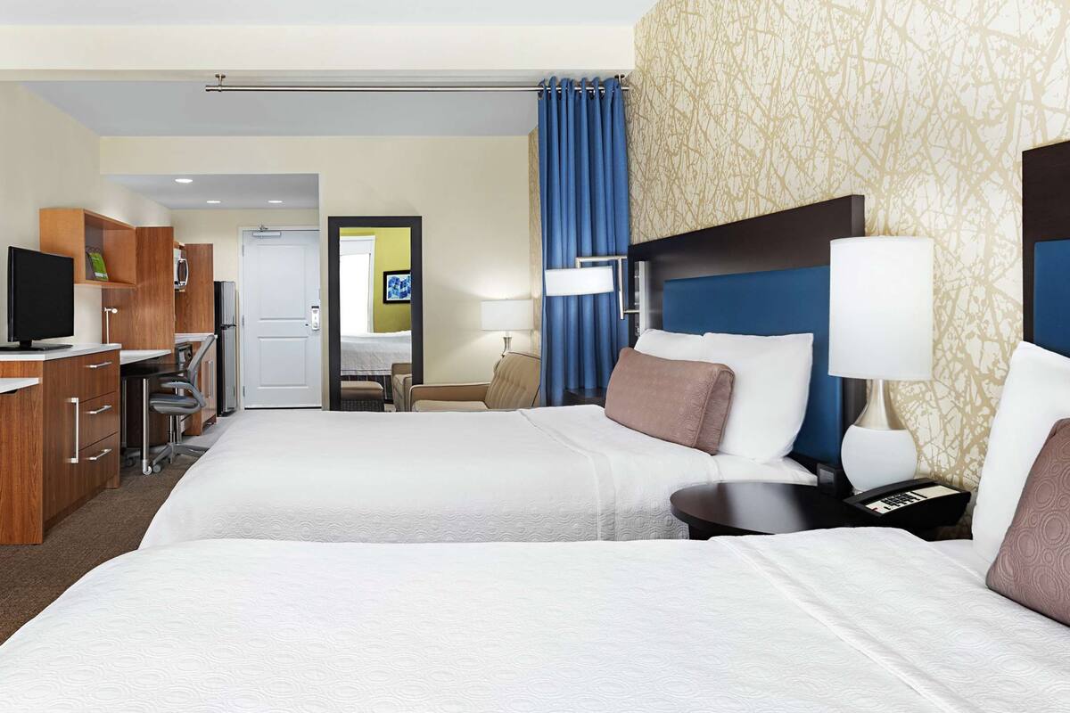 Une chambre d’hôtel avec deux lits, des armoires en bois, un bureau et un téléviseur.