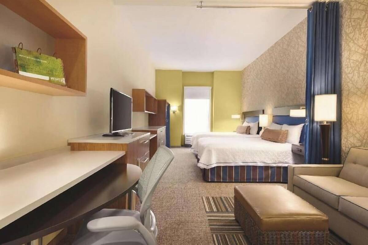 Une chambre d’hôtel équipée d’un bureau, de deux lits, d’une télévision, d’un canapé et d’une fenêtre avec des rideaux.