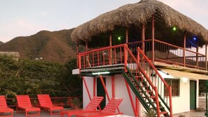 A hot tub with a tropical design, a thatched-roof structure, and red chairs. - Hostal Acuarius (Santa Marta)