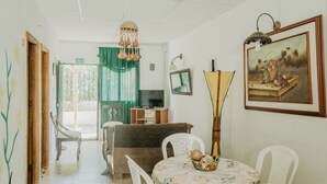 A living room with a television, a dining table with chairs, a sofa, and a painting on the wall. - Hostal Acuarius (Santa Marta)