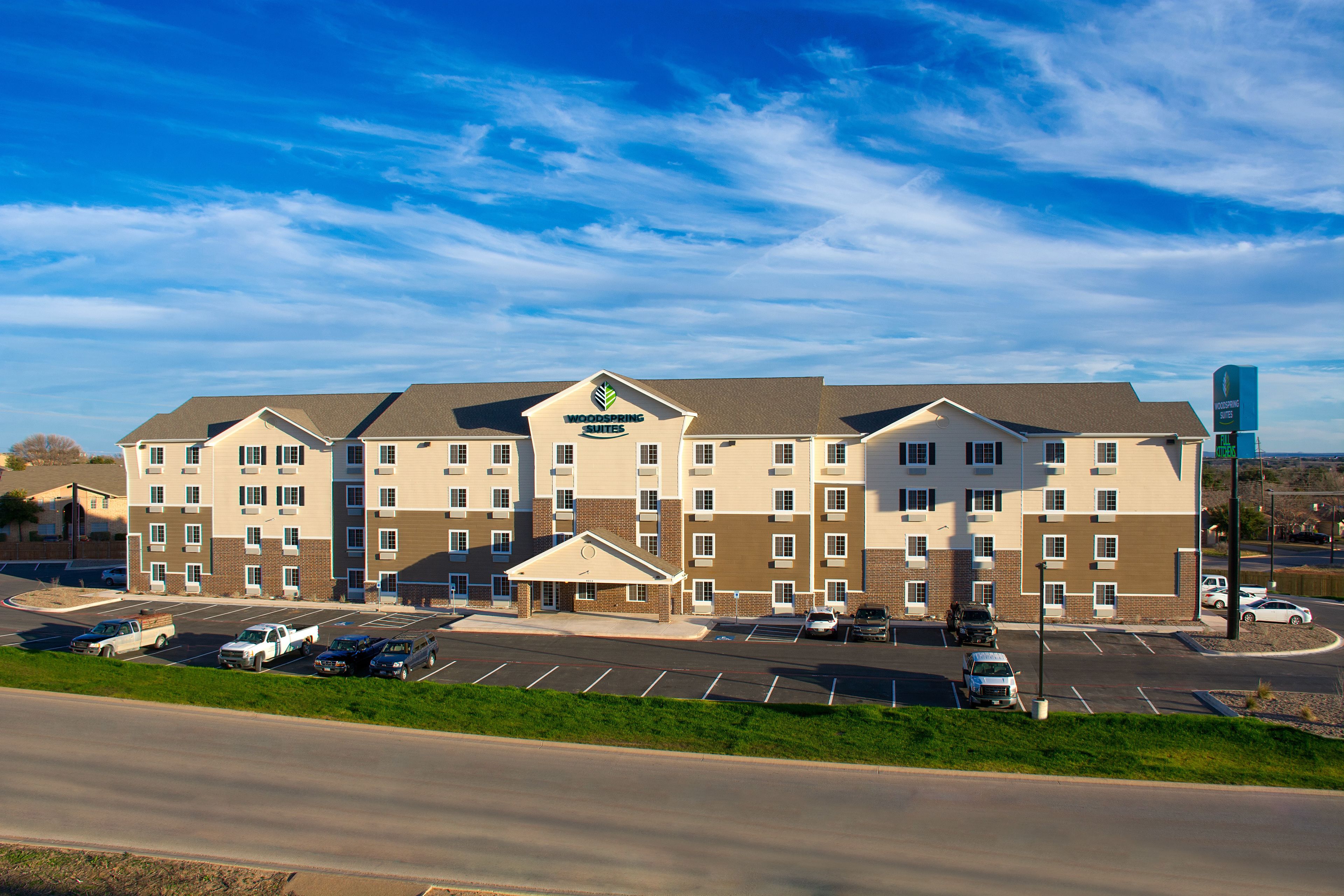 A multi-story hotel with a central entrance, parking lot, and a clear sky.