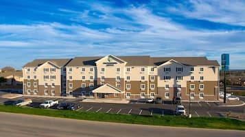 A multi-story hotel with a central entrance, parking lot, and a clear sky.
