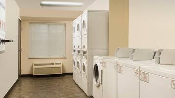 A laundry room with stacked washers and dryers, a vent, and a window with blinds.