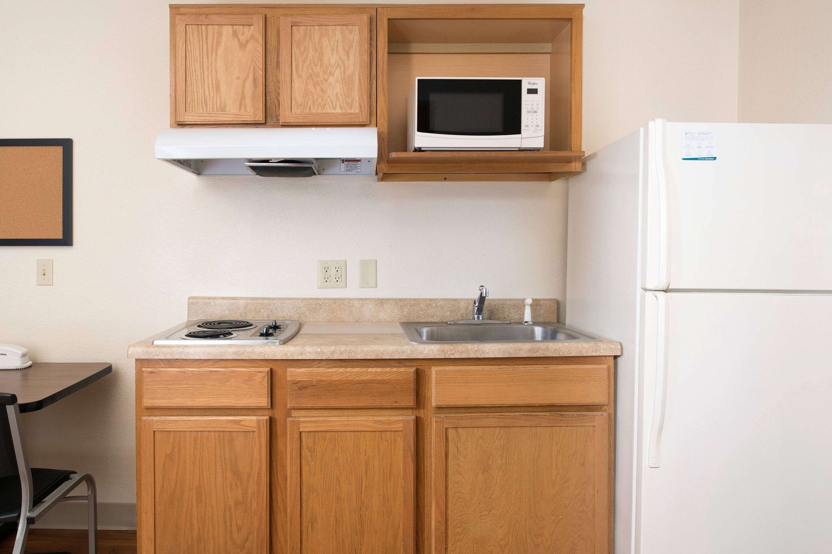 A compact kitchen with wooden cabinets, a microwave, a sink, and a refrigerator.