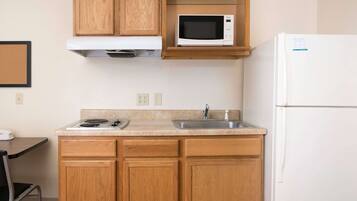 A compact kitchen with wooden cabinets, a microwave, a sink, and a refrigerator.