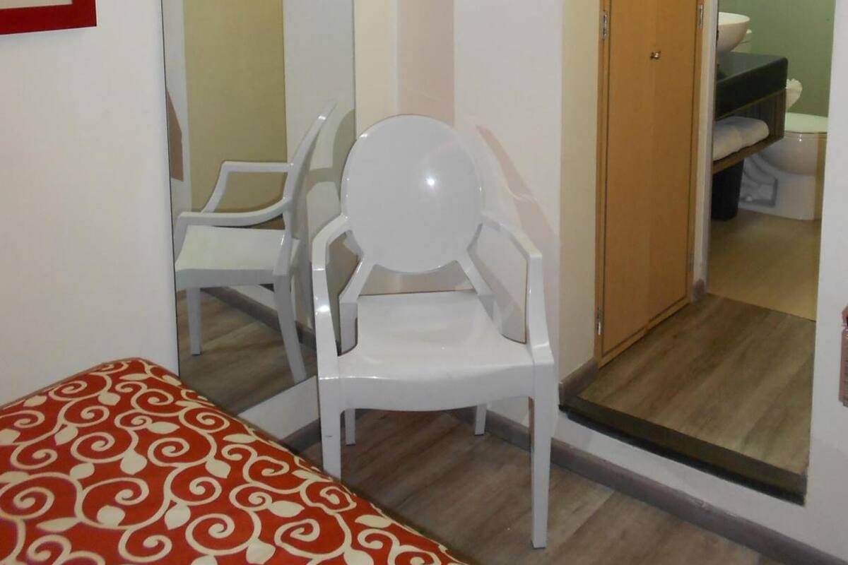 Una habitación con cama, una silla, un espejo, una puerta que da a un baño y una mesita.