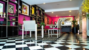 A room with a checkered floor, a white chair, a dining table with chairs, and a bookshelf filled with books and decorative items.