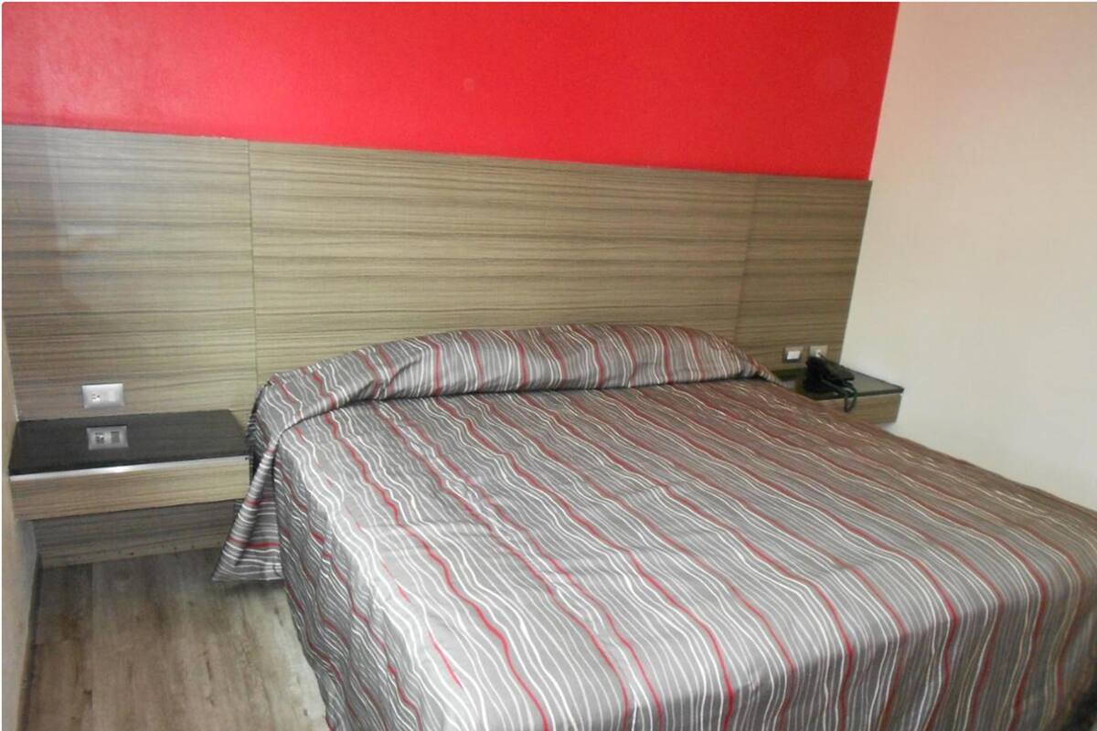 Una cama con una colcha a rayas, una mesita de noche y una pared roja.