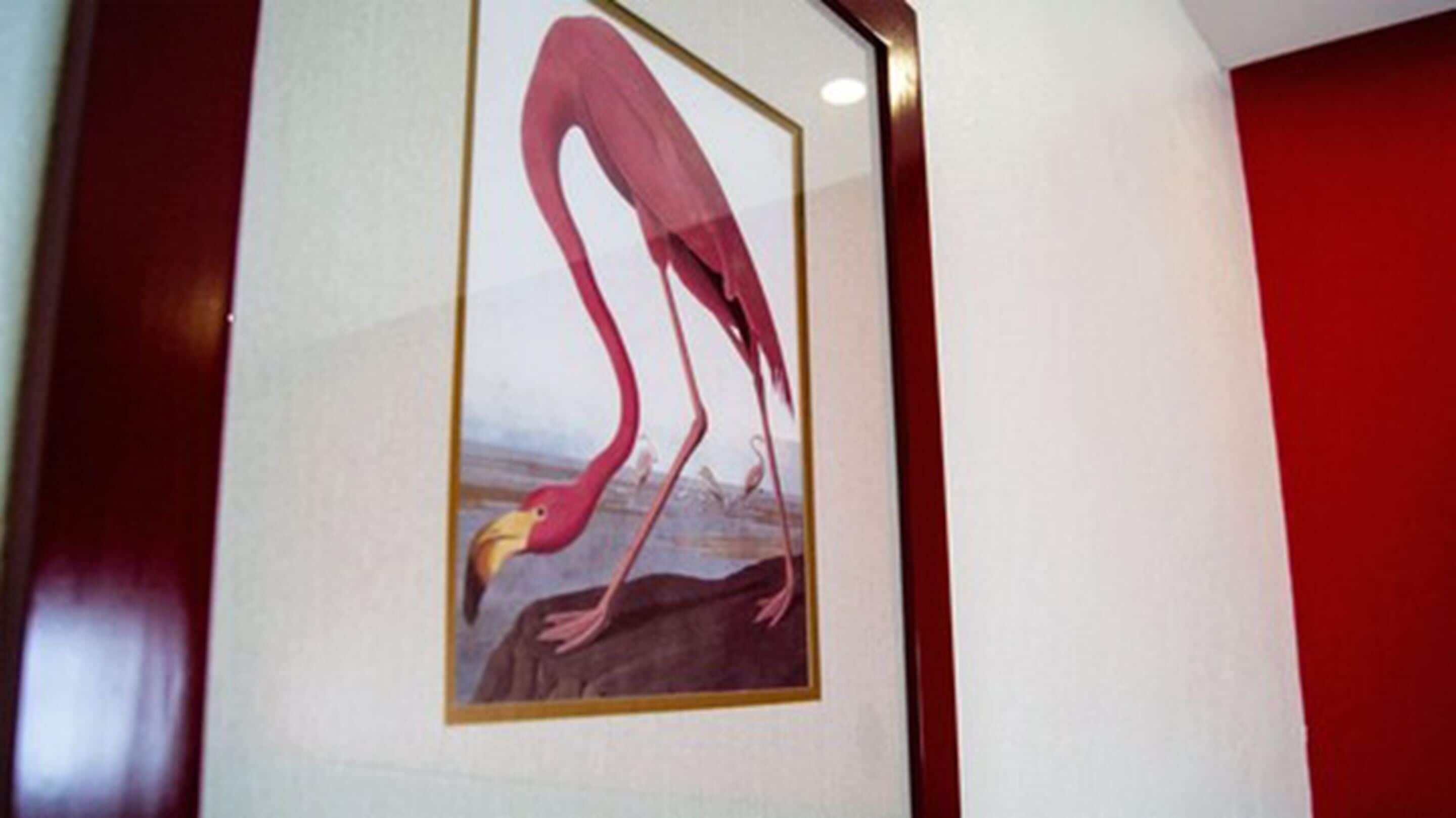A framed picture of a flamingo on a rock.