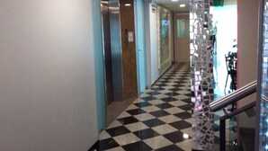 Um corredor com chão quadriculado, um elevador e uma divisória de vidro decorativa.