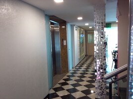 A hallway with a checkered floor, an elevator, and a decorative glass partition.