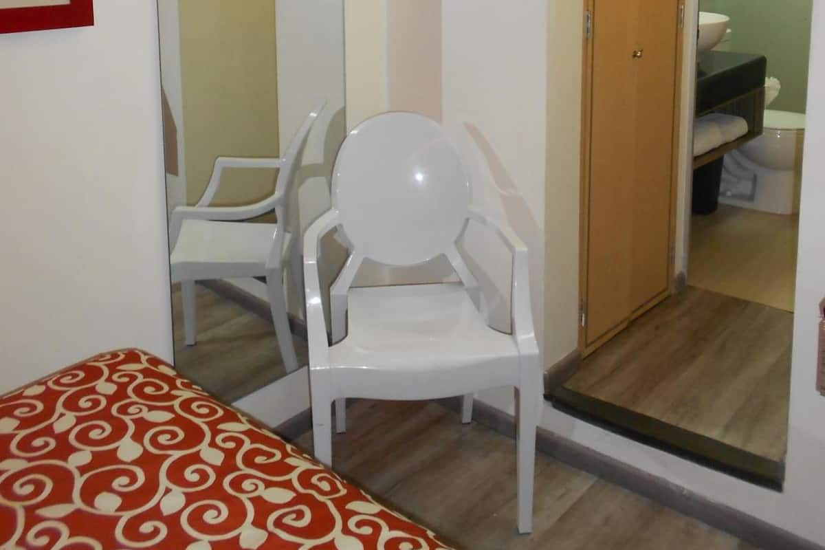 Una habitación con cama, una silla, un espejo, una puerta que da a un baño y una mesita.