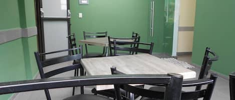 A dining area with a green wall, a whiteboard, and a door marked "SALIDA DE EMERGENCIA".