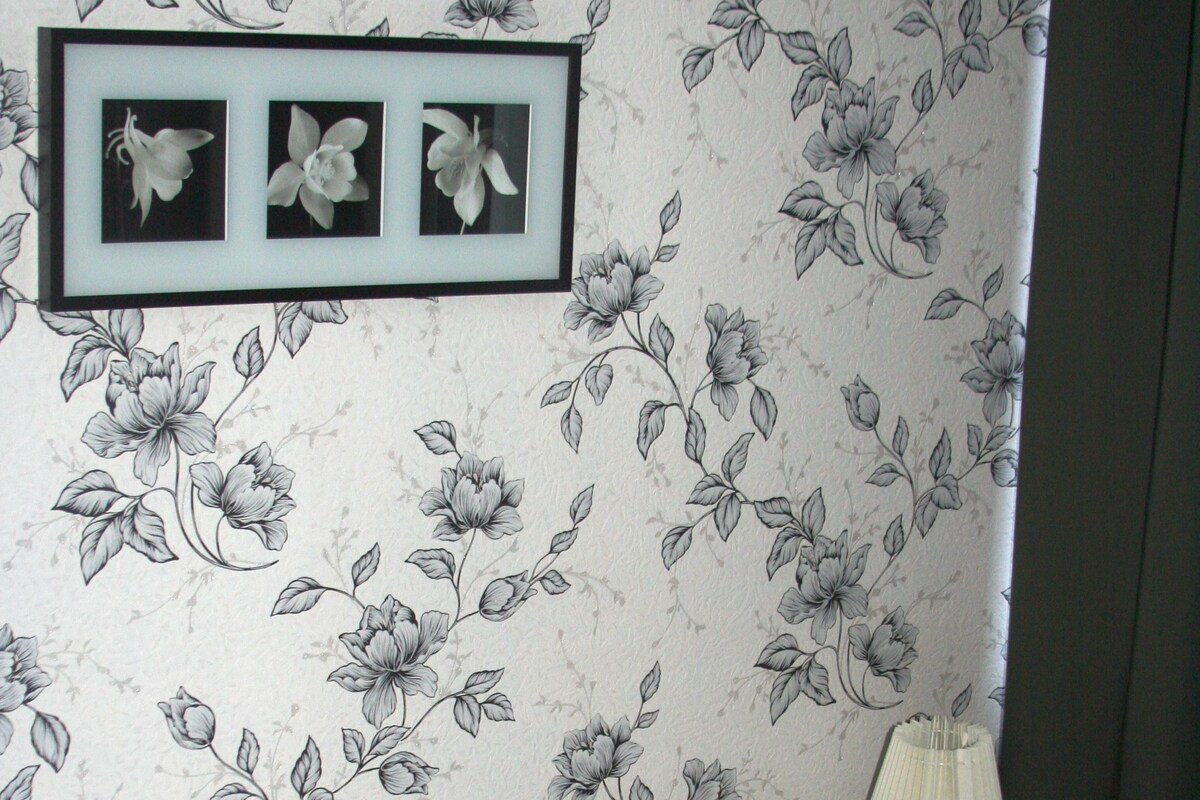 A bedroom with a floral wallpaper, a bed with striped bedding, and a framed picture above the bed.