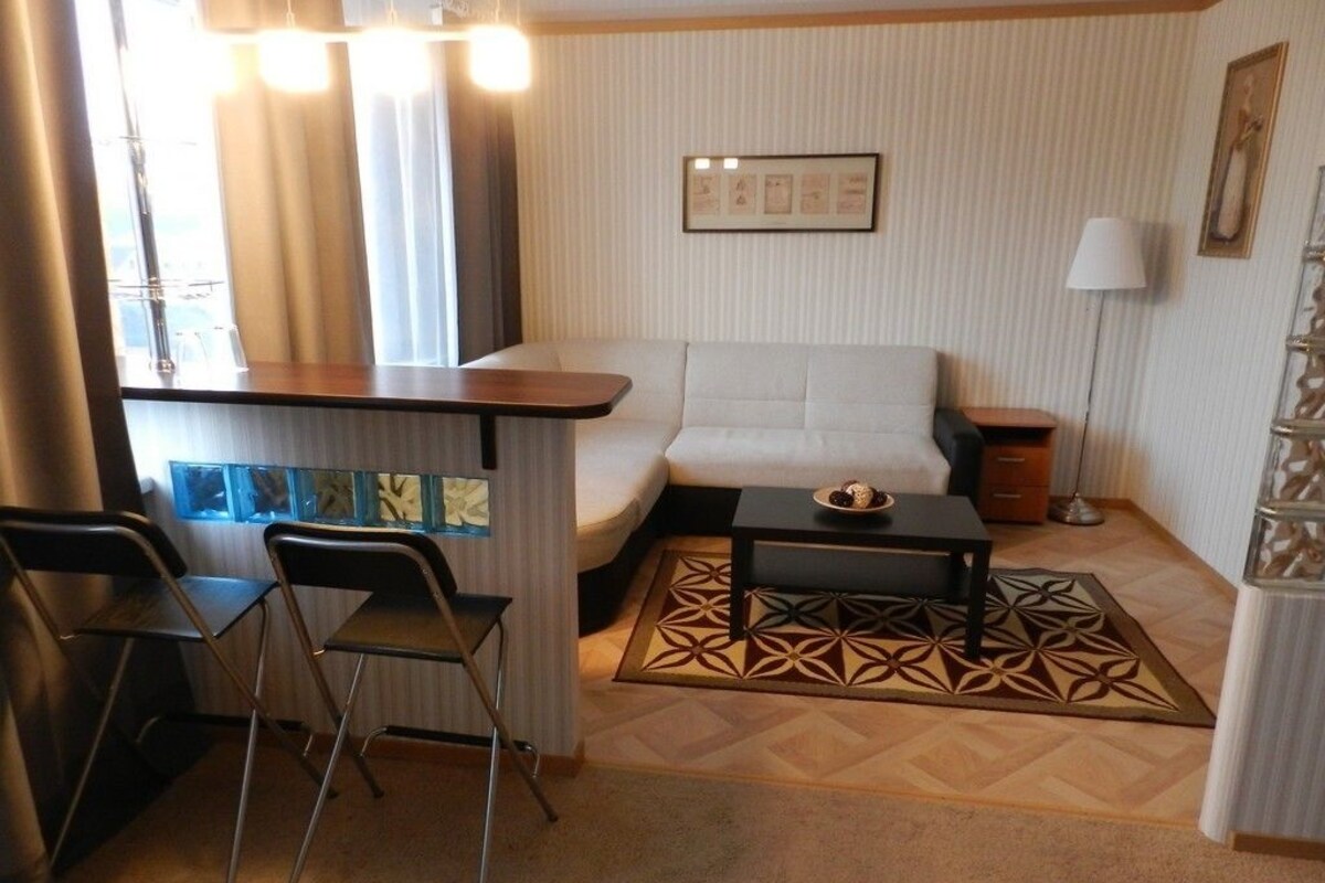 A compact living area with a sofa, a small table, and two chairs. A decorative rug is on the floor, and there is a framed picture on the wall.