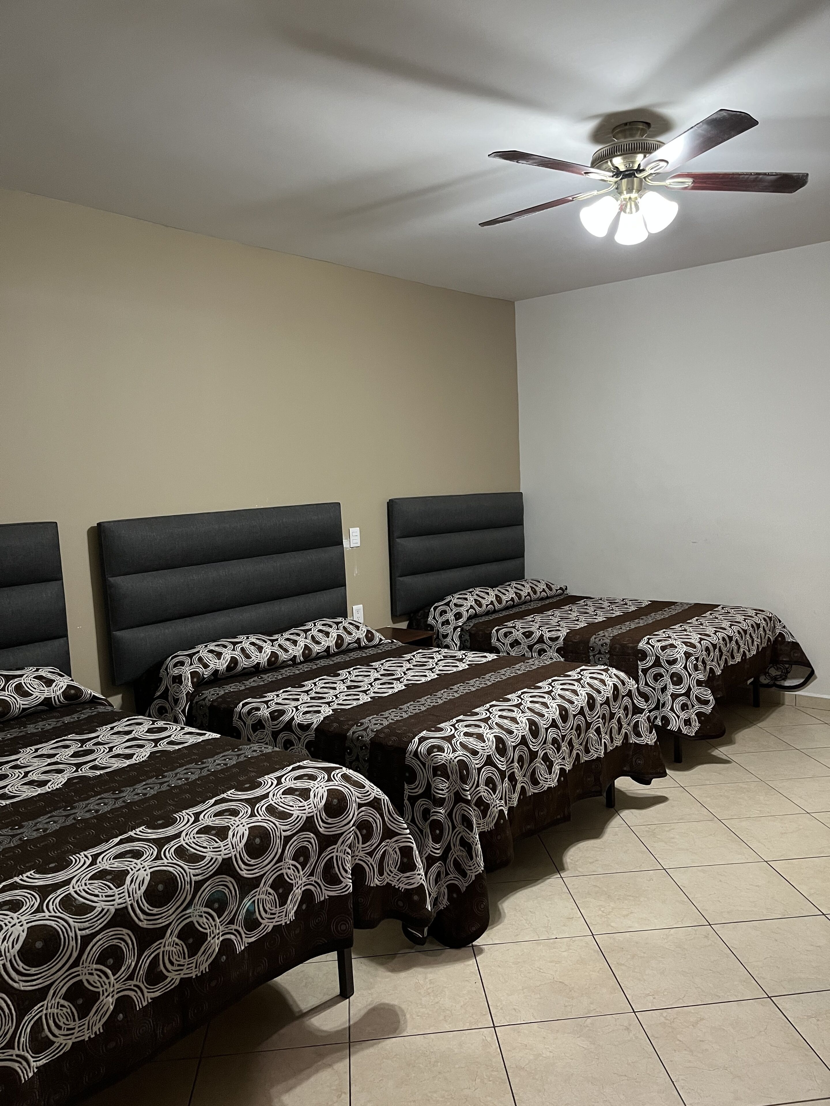 A hotel room with four beds, a ceiling fan, and a tiled floor.