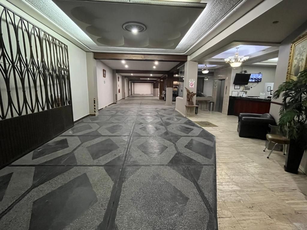 A hotel lobby with a patterned floor, a reception desk, a television, and a plant.