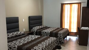 Una habitación de hotel con dos camas, un ventilador de techo, una ventana con cortinas y una mesita.
