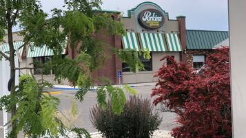 Ein Perkins Restaurant & Bakery mit einem grün-weiß gestreiften Vordach, einem Backsteinhaus und einem Parkplatz mit Bäumen und Sträuchern.