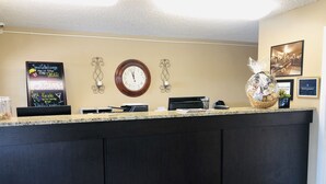 A reception desk with a clock, a chalkboard with event information, and a framed picture on the wall. - Budget Motel (Burley)