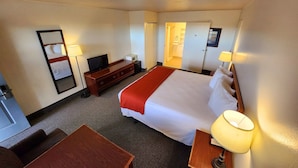 A hotel room with a bed, a desk, a TV, a microwave, and a bathroom door. - Budget Motel (Burley)