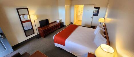 A hotel room with a bed, a desk, a TV, a microwave, and a bathroom door.