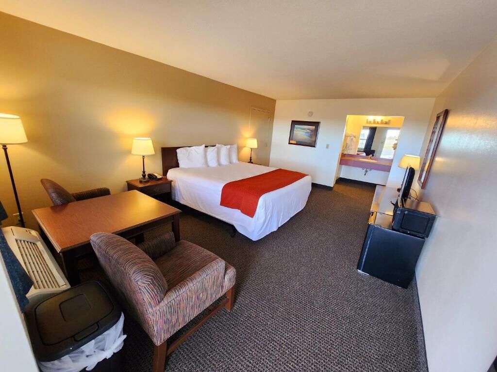 A hotel room with a bed, desk, chair, and a small table.