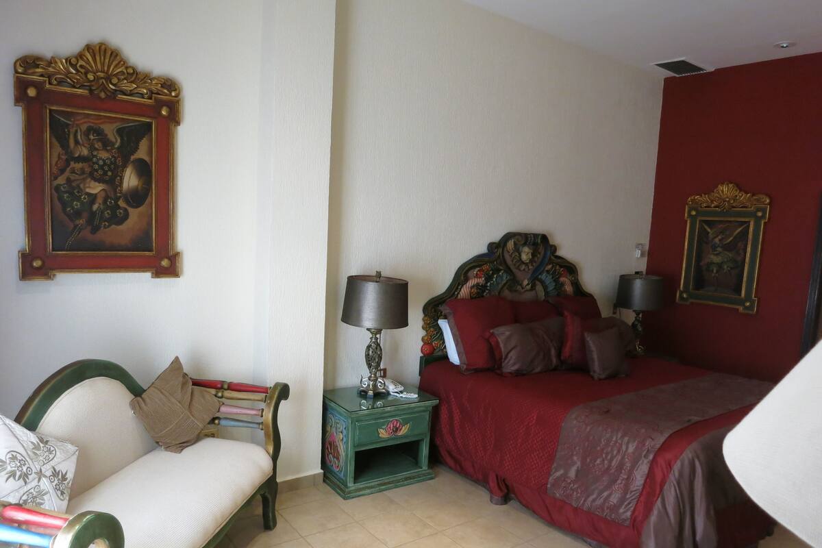 A bedroom with a bed, a nightstand, a chair, and a wall with a framed picture.