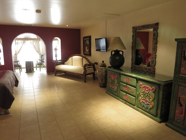 Habitación de hotel con sofá, televisor, lámpara, aparador decorativo y un espejo grande.