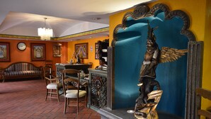 Un hall de hotel con mostrador de recepción, zona de estar con sillas y sofá, un muro decorativo con una estatua y un reloj en la pared.