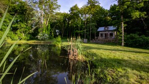 A rustic cabin surrounded by lush greenery and a pond.