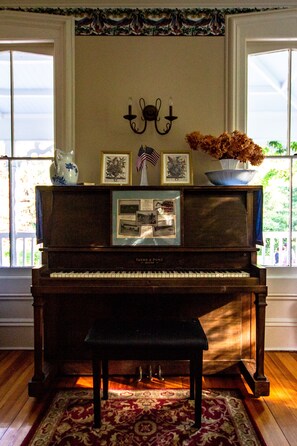 A grand piano with a bench, a decorative vase with flowers, framed pictures, and a wall-mounted candle holder.