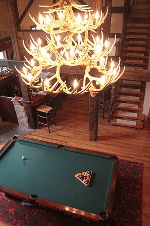 A pool table with a triangular bally in the center, a wooden bar area, and a staircase with a wooden railing.