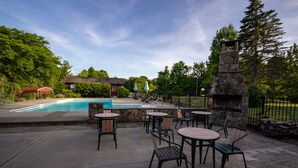 An outdoor patio area with a pool, stone fireplace, and seating arrangements.