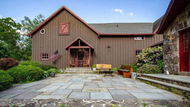 A wooden building with a stone extension, a stone patio, and a bench.