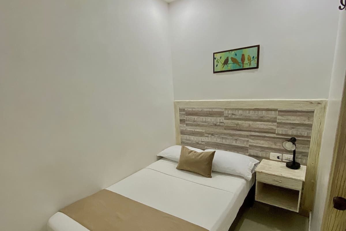 A neatly made bed with a brown throw, a nightstand with a lamp, and a wall-mounted picture of birds.