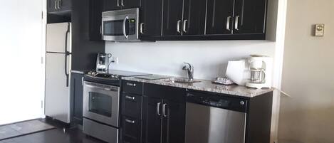 Een moderne keuken met zwarte kastjes, roestvrijstalen apparatuur, een magnetron, een koffiezetapparaat en een vaatwasser.
